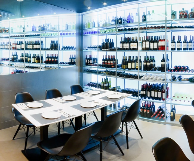 Vitrinas acristaladas e iluminadas con la selección de vinos de Bar Perico, junto a una mesa preparada